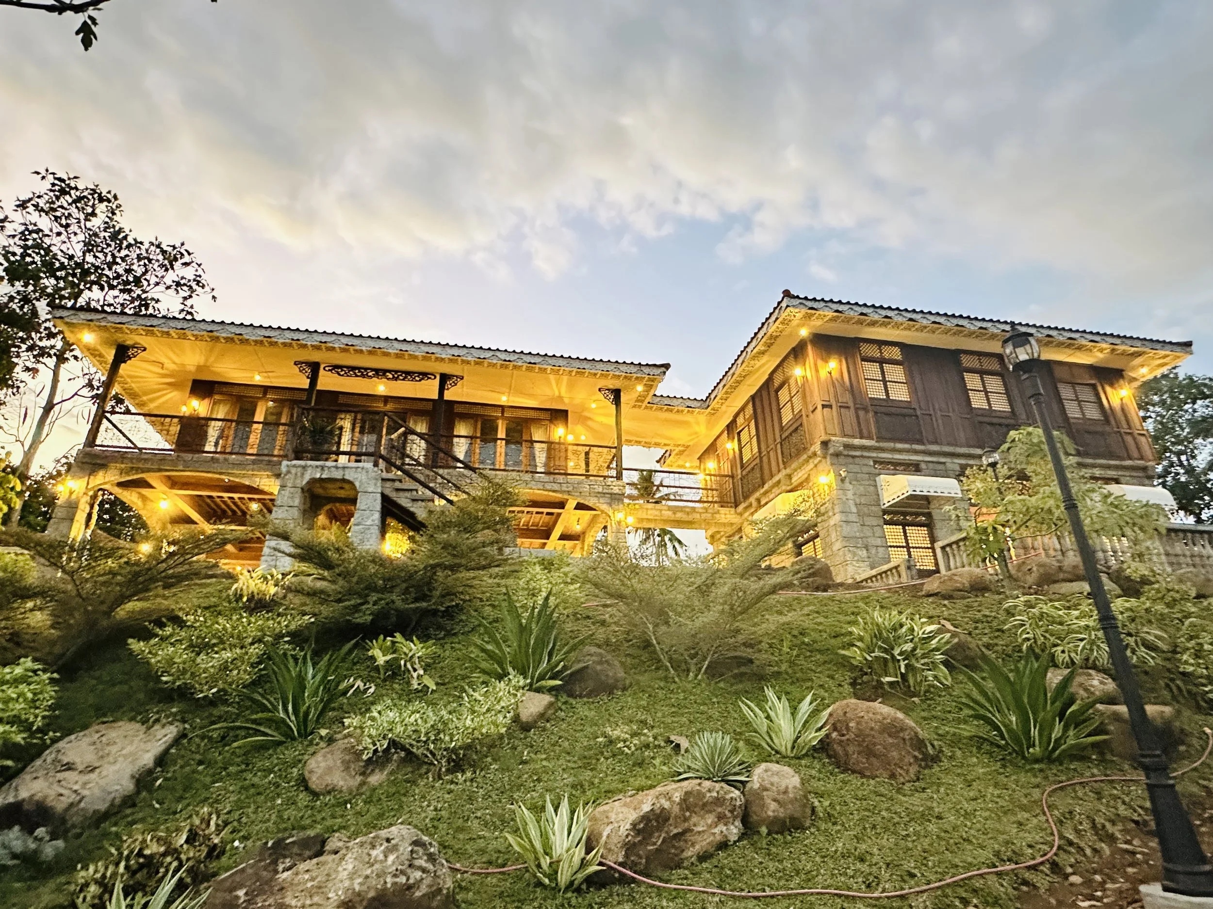 The bahay na bato great house glowing at dusk above the gardens