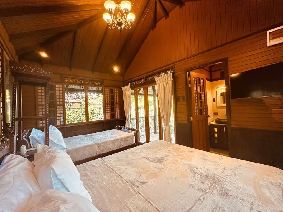 A heritage bedroom with carved wooden beds, white linens and a warm chandelier