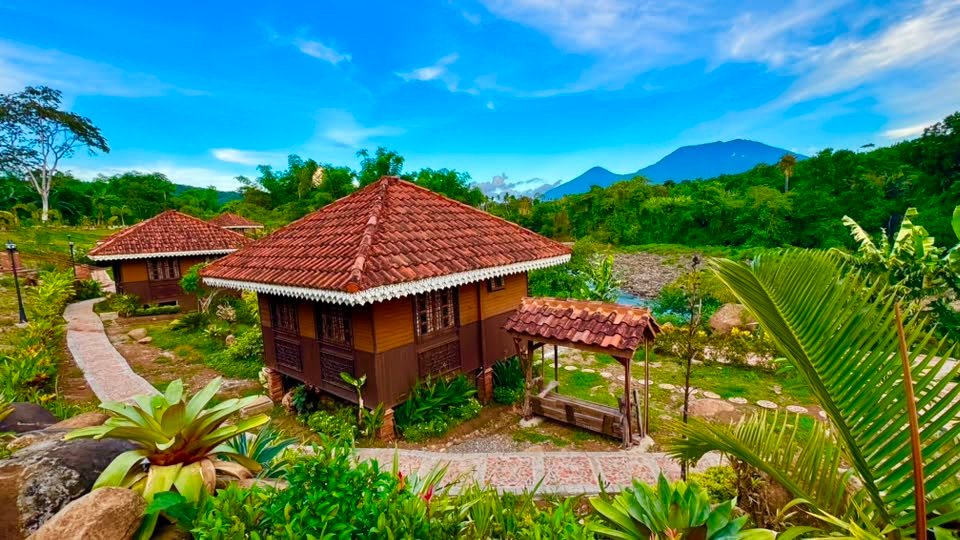 A riverside kubo with the mountain rising beyond the treeline